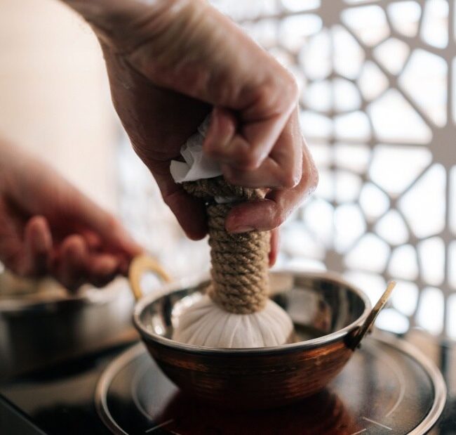 The hands of an Ayurvedic practitioner preparing a Shirodhara treatment.