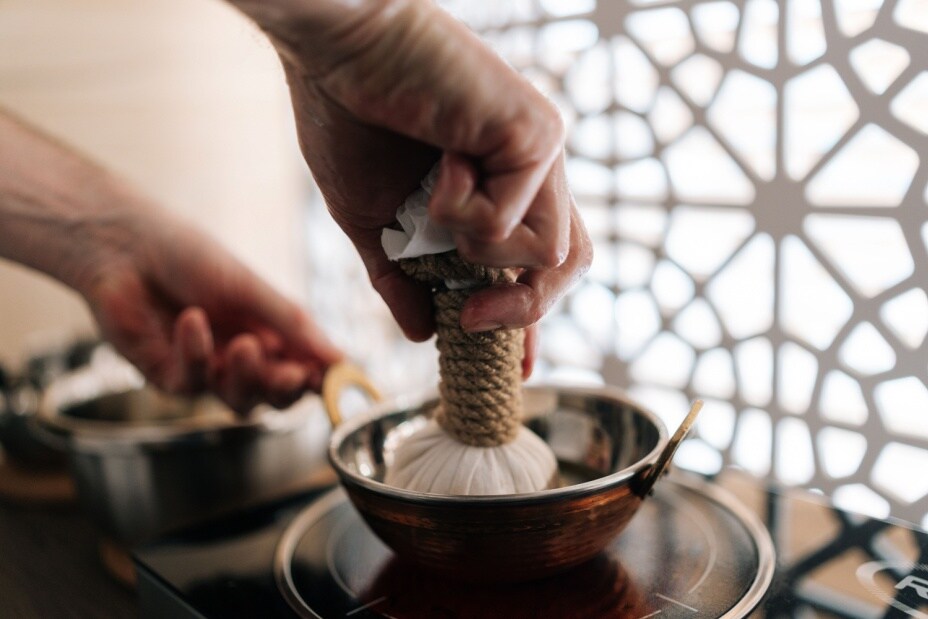 The hands of an Ayurvedic practitioner preparing a Shirodhara treatment.