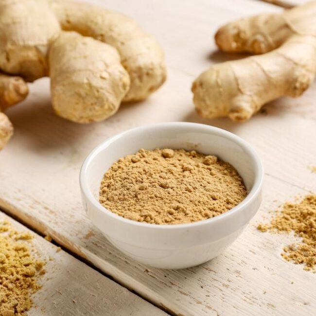 Fresh ginger root and dried ginger powder arranged on a wooden table.