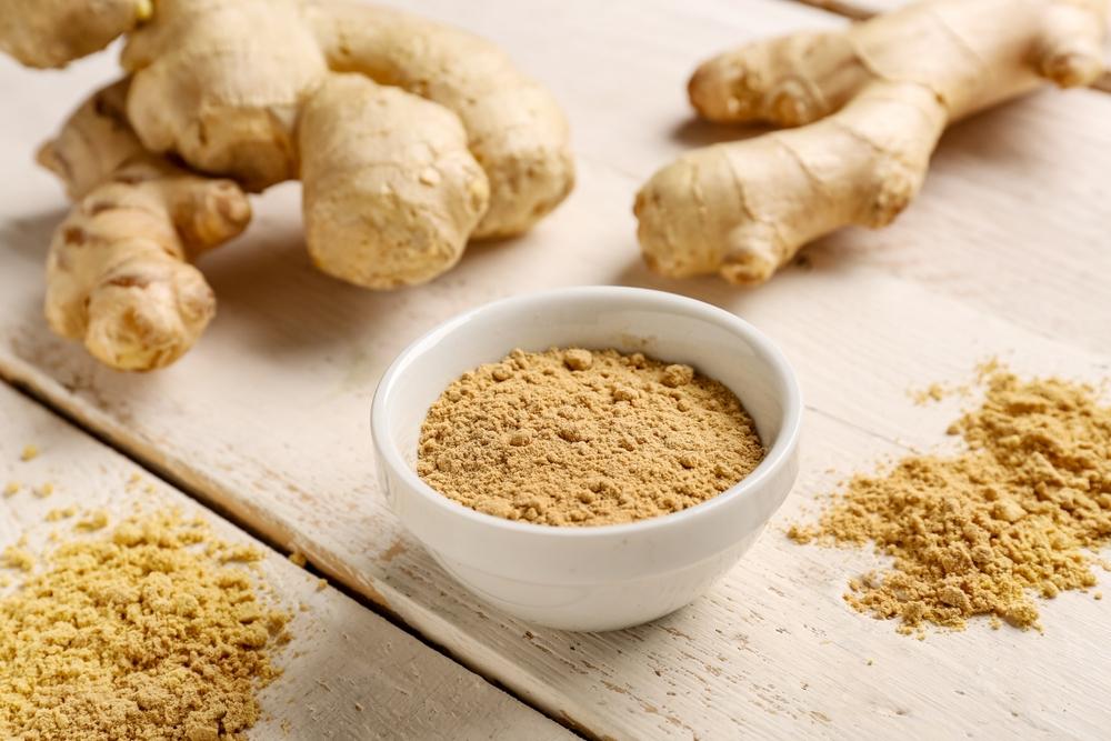 Fresh ginger root and dried ginger powder arranged on a wooden table.