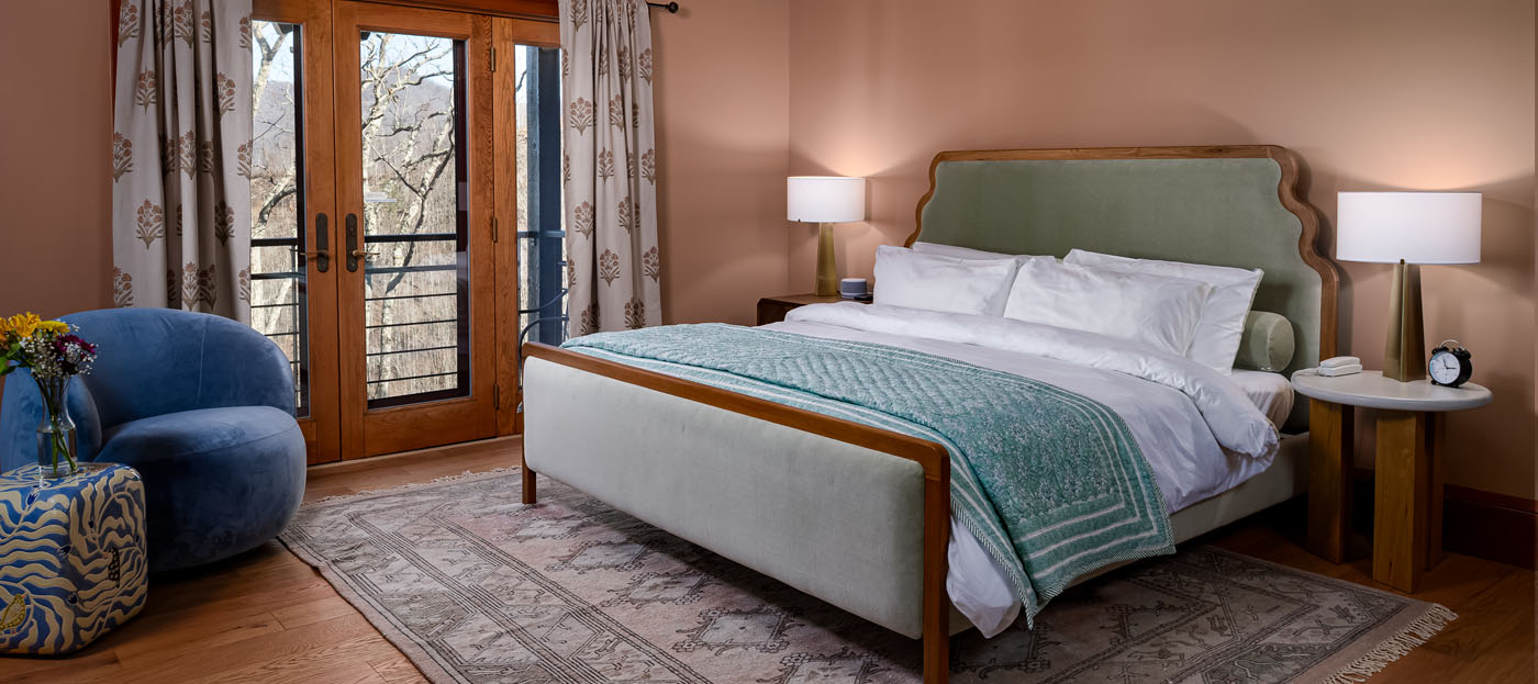 Beautiful guest room interior of the Green Tara room at SoHum Mountain Healing Resort, showing a bed next to a balcony overlooking the mountains