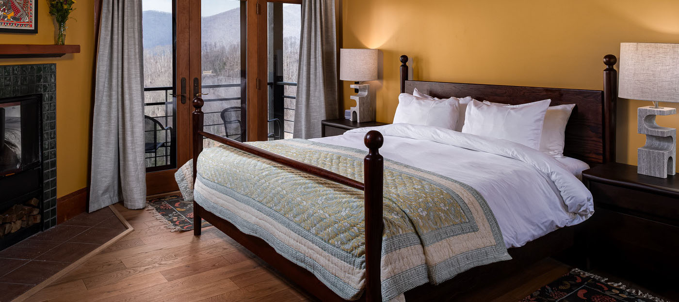 Beautiful guest room interior of the Laxmi room at SoHum Mountain Healing Resort, showing a bed next to a balcony overlooking the mountains