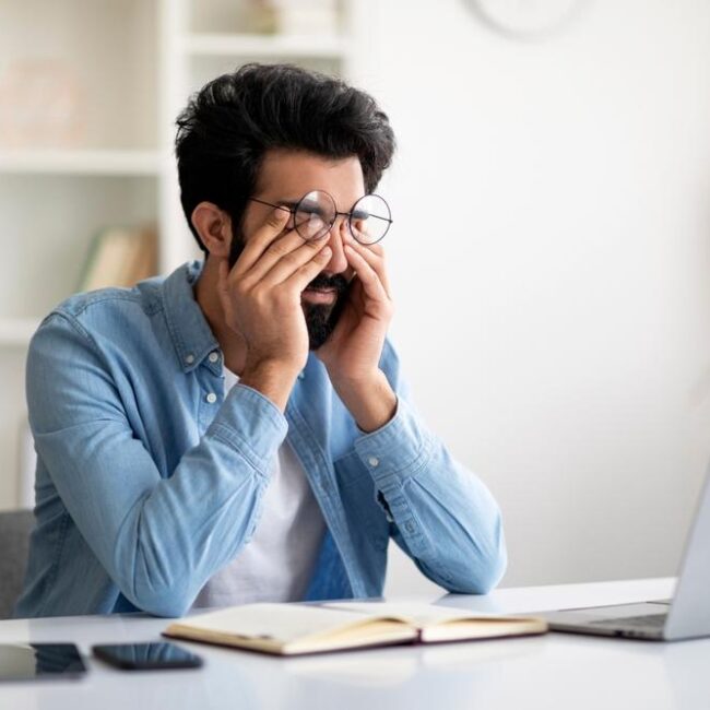 A young man experiencing burnout buries his head in his hands at his desk.
