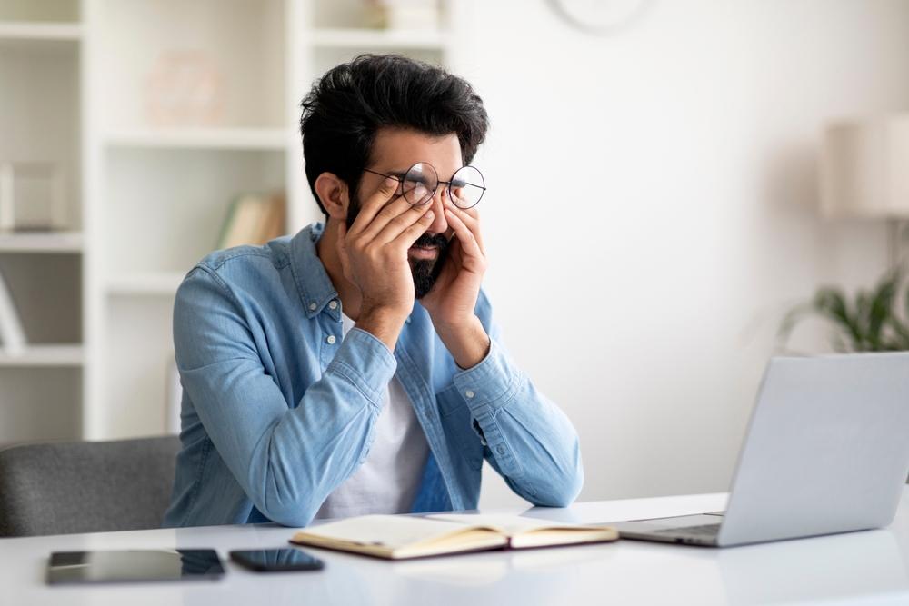 A young man experiencing burnout buries his head in his hands at his desk.