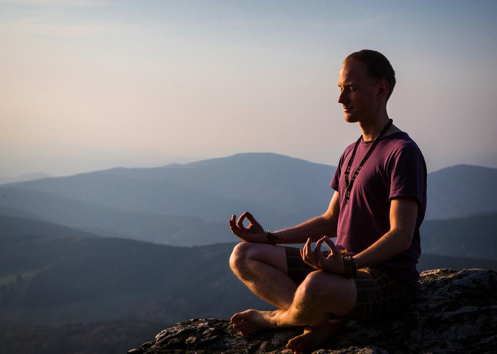 A man meditates atop a rock in a mountainous area.