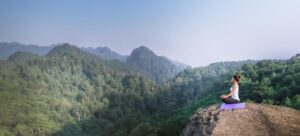 A woman meditates in a lush, mountain setting.