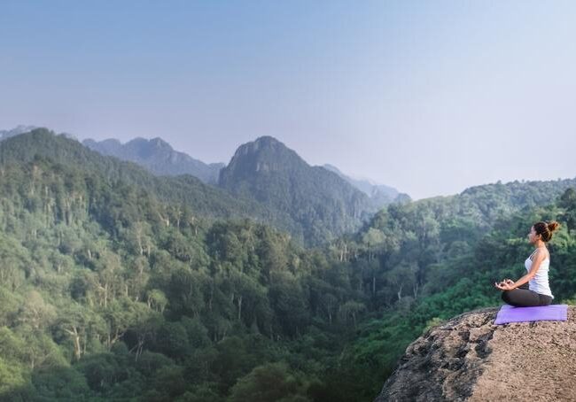 A woman meditates in a lush, mountain setting.