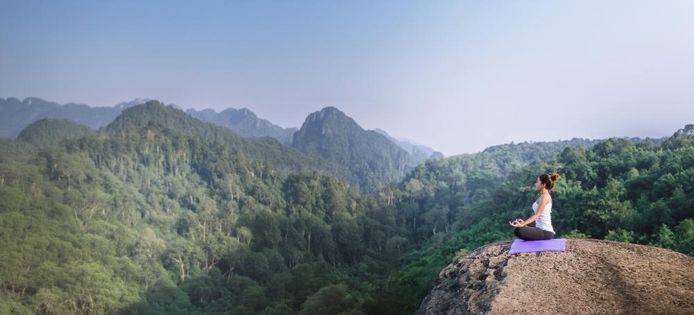 A woman meditates in a lush, mountain setting.
