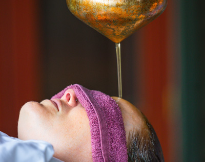 woman getting warm oil poured on her forehead during a shirodhara treatment at SoHum Mountain Healing Resort