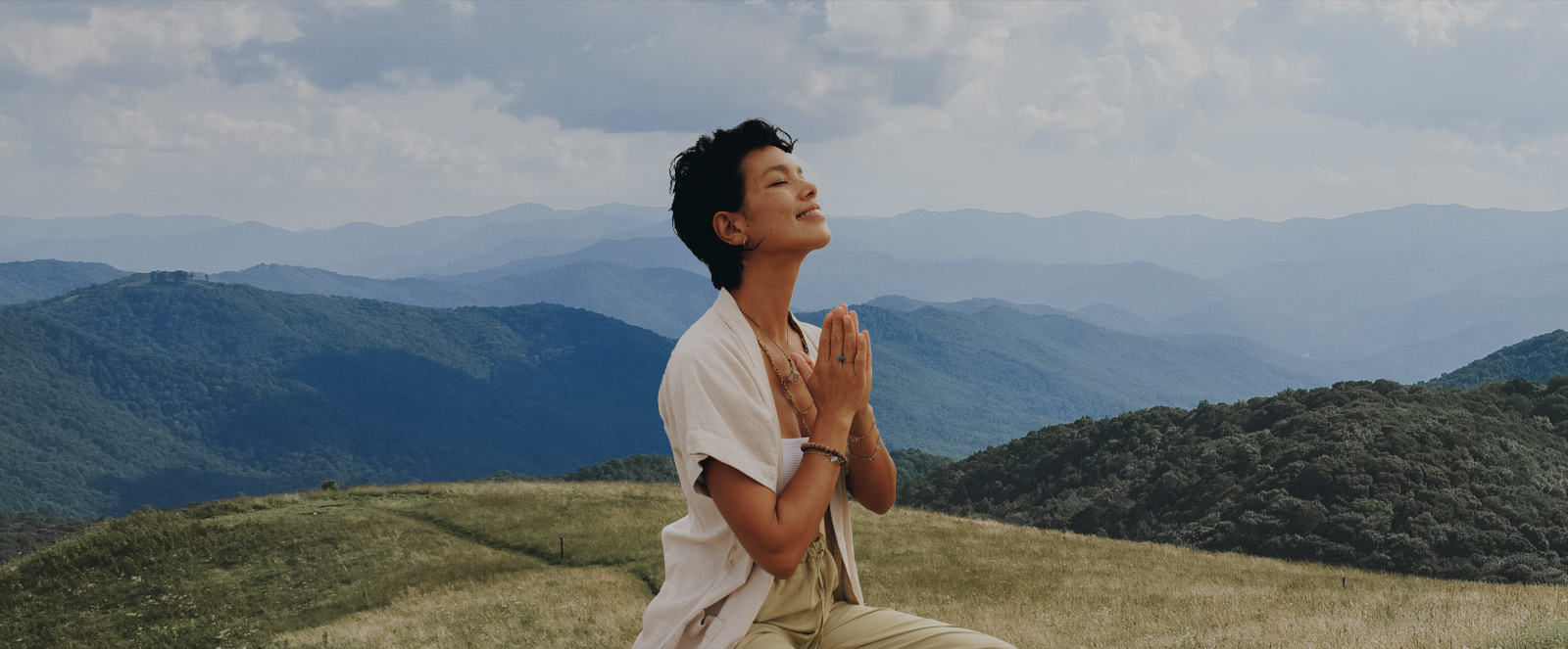 woman sitting in front of the blueridge mountains with hands in prayer