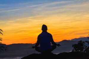 A person meditating on a mountain top with the sunrising around them.