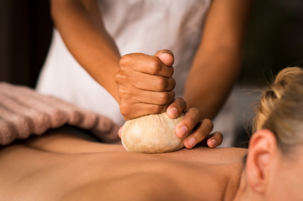 Close-up of a therapist’s hands as she gives an ayurvedic aroma pinda sweda massage to a senior woman.