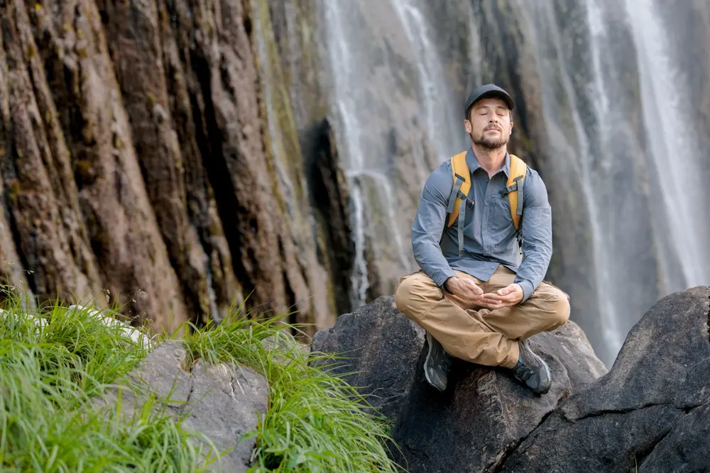 A young hiker stops to meditate in the beautiful mountains.