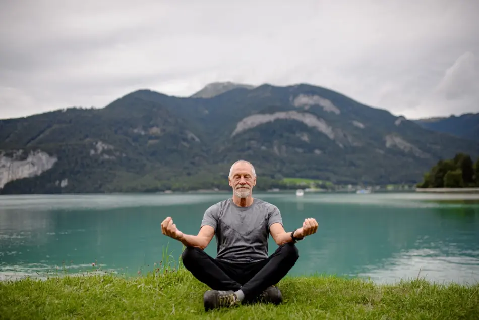 A senior man meditates in an outdoor mountain setting, setting intentions for his day.