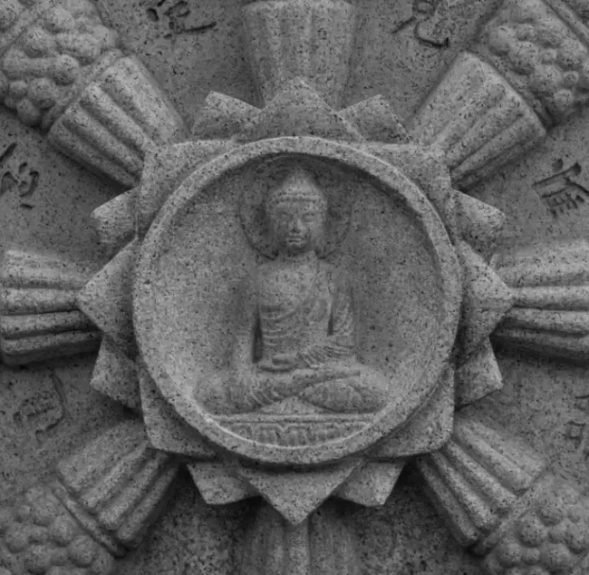 A stone dharma wheel with an image of Buddha in the center.