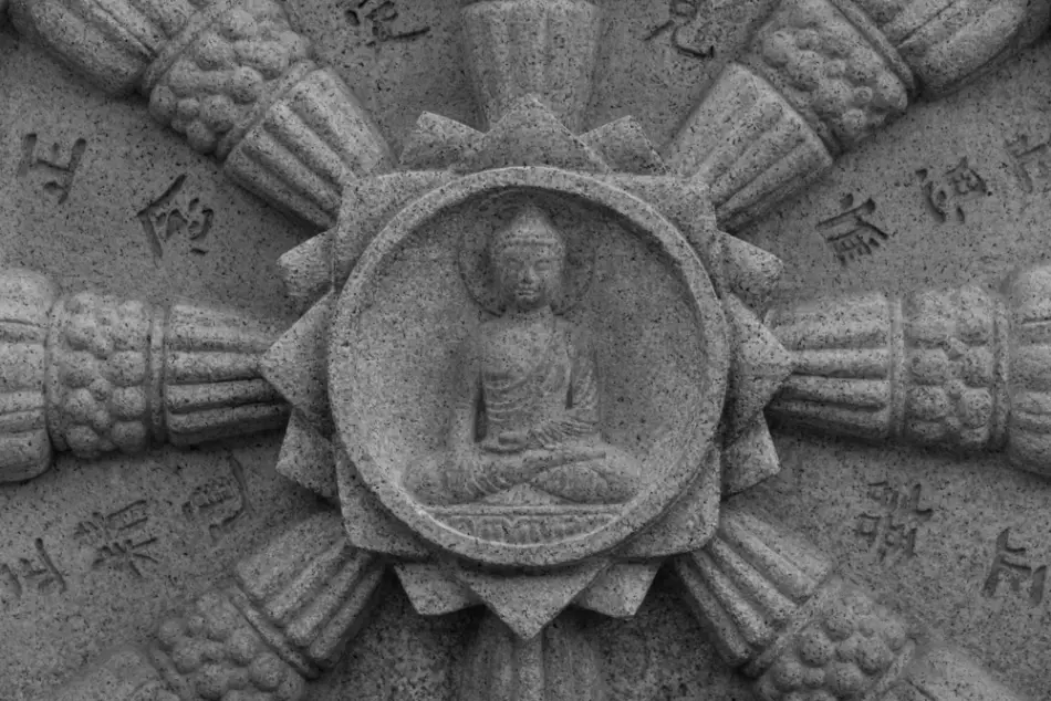 A stone dharma wheel with an image of Buddha in the center.