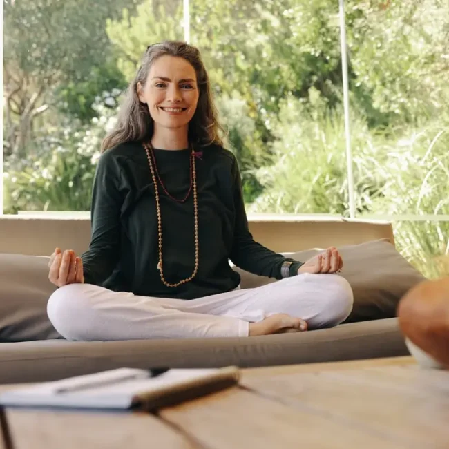 A woman engages in a Vedic meditation practice in front of a window to nature.