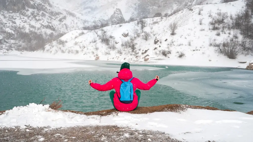 A woman meditates outdoors in the mountains in winter.