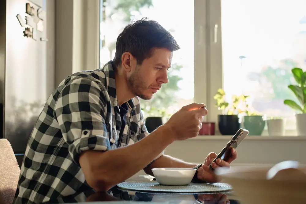 A man is distracted by his cellphone during breakfast.