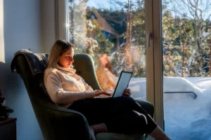 A young woman struggles to work on a laptop on a snowy winter day.