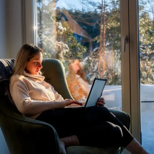A young woman struggles to work on a laptop on a snowy winter day.