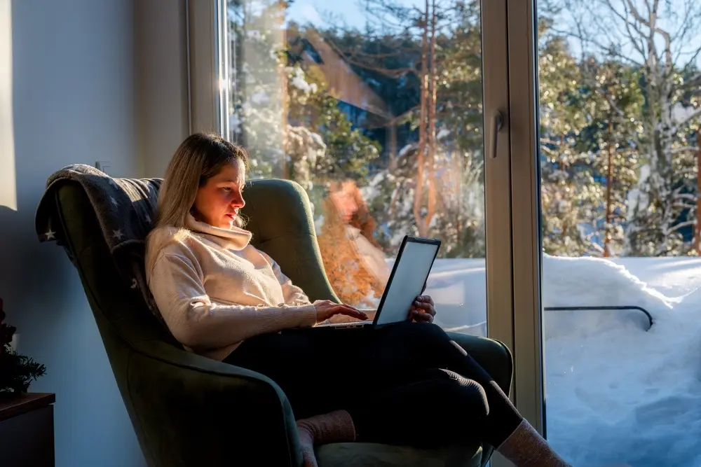 A young woman struggles to work on a laptop on a snowy winter day.
