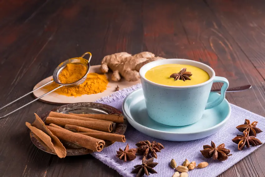 A warm cup of tea surrounded by various spices.
