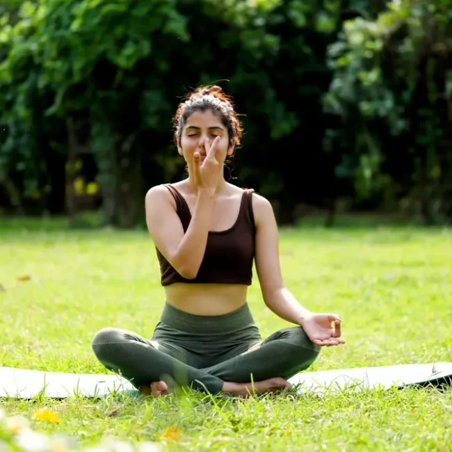 A woman sitting outdoors practicing alternate nostril breathing