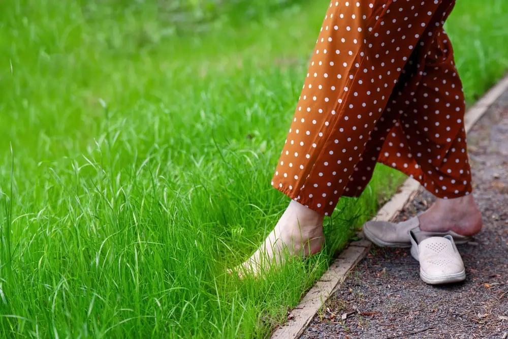 A woman walking barefoot in the grass as a grounding practice.