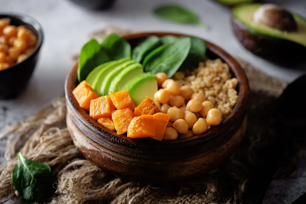 A bowl of spinach, quinoa, sweet potato, and avocado