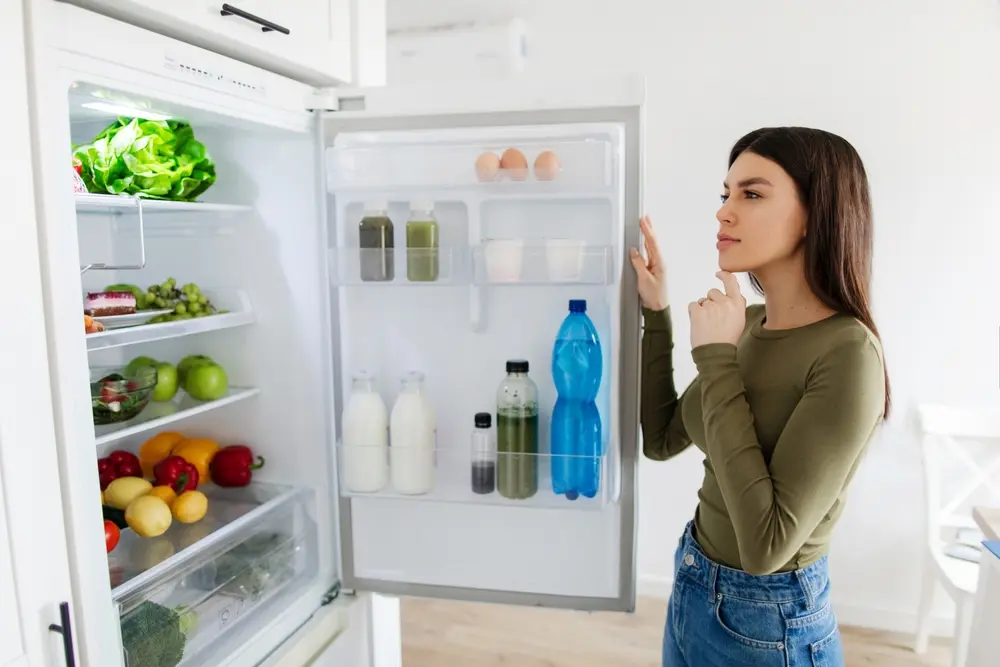A woman in front of a fridge choosing meal ingredients